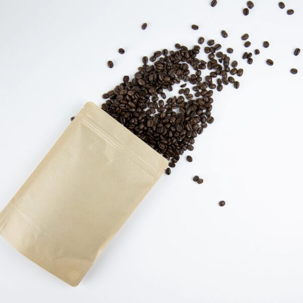 Top view of roasted coffee beans spilling from a kraft paper pouch on a clean white background, Minimal studio composition highlighting packaging design and organic product concept for branding and food marketing